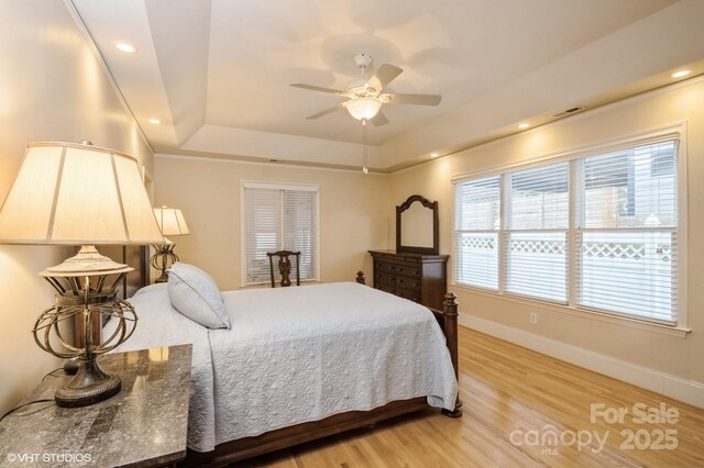 bedroom with recessed lighting, light wood finished floors, baseboards, and a raised ceiling