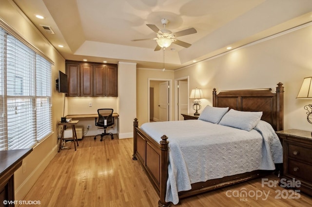 bedroom with visible vents, baseboards, built in study area, a tray ceiling, and light wood-style flooring