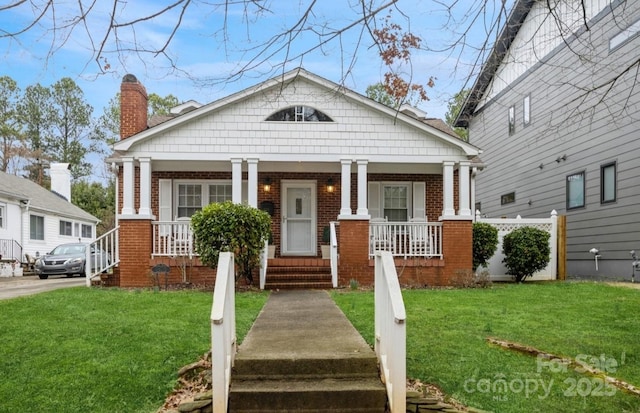 bungalow-style house with a chimney, covered porch, a front lawn, and brick siding