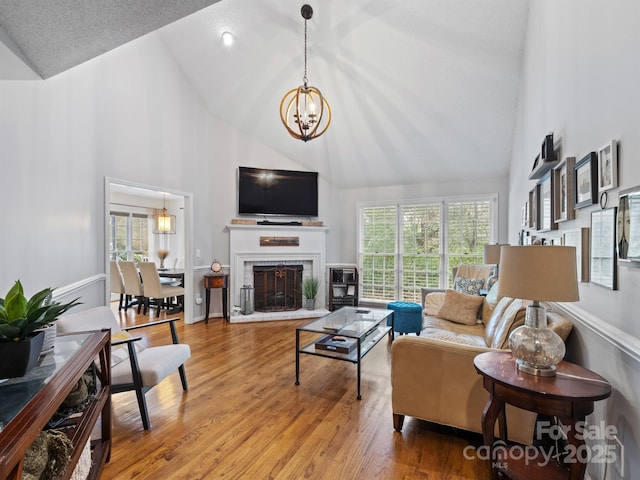 living room with high vaulted ceiling, a brick fireplace, wood finished floors, and an inviting chandelier