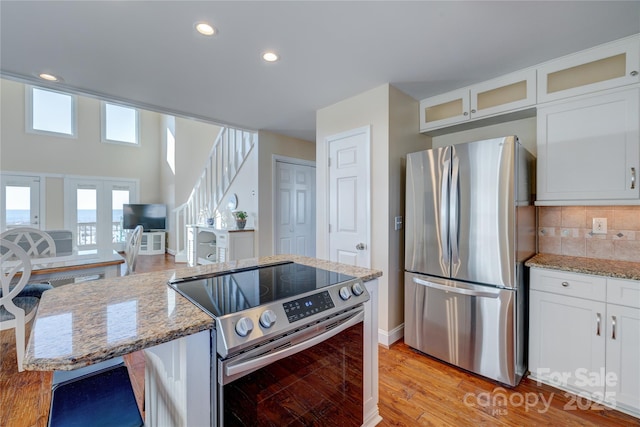 kitchen with white cabinetry, tasteful backsplash, light stone counters, stainless steel appliances, and light hardwood / wood-style floors