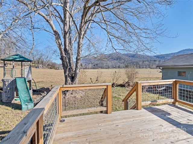 wooden terrace featuring a playground, a mountain view, and a rural view