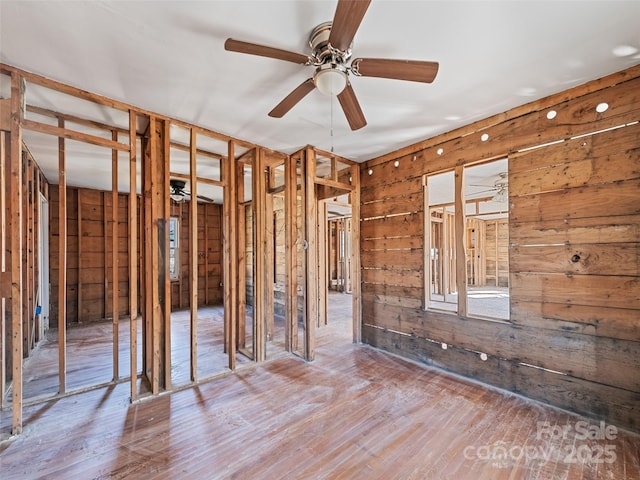 misc room featuring ceiling fan, hardwood / wood-style floors, and wood walls