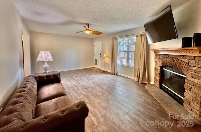 living area featuring a textured ceiling, baseboards, wood finished floors, and a stone fireplace