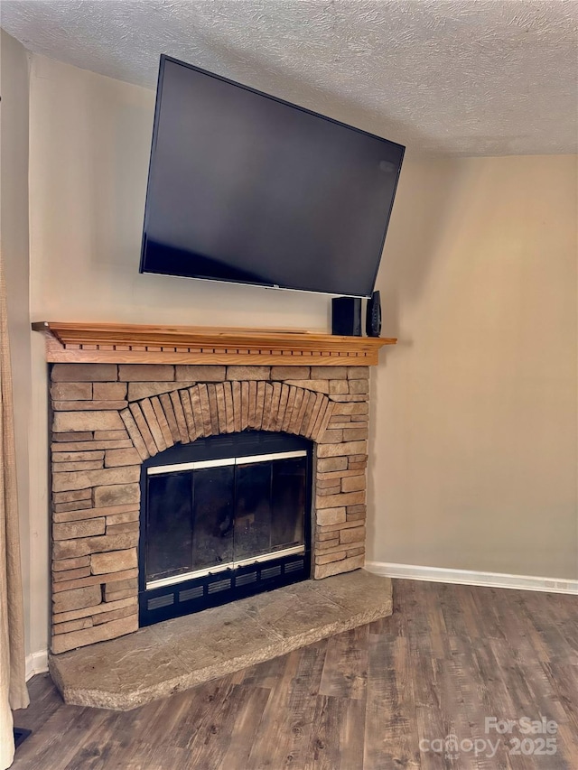 details with a textured ceiling, a stone fireplace, wood finished floors, and baseboards