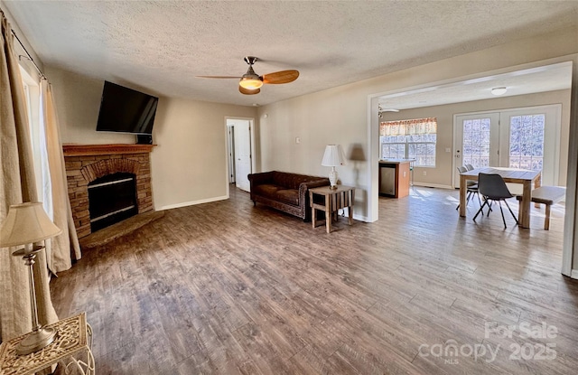 living area with a textured ceiling, ceiling fan, a fireplace, and wood finished floors