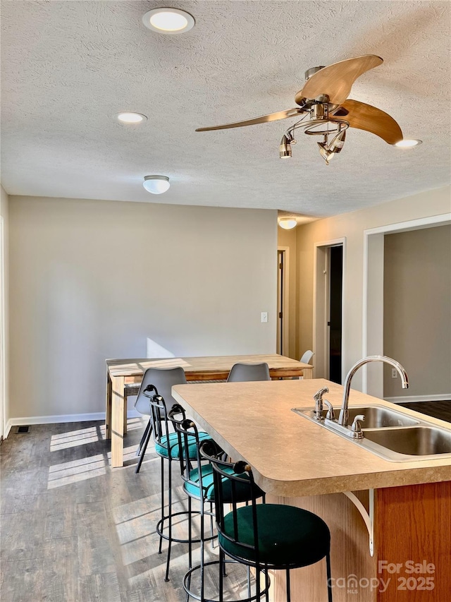 kitchen with ceiling fan, a textured ceiling, wood finished floors, a sink, and baseboards