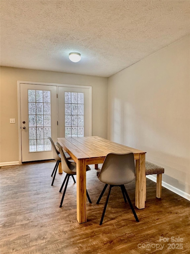 dining space with a textured ceiling, baseboards, and wood finished floors