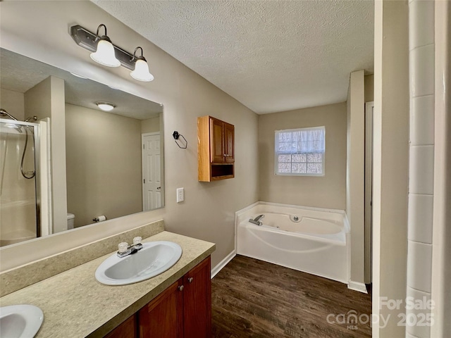 bathroom with double vanity, wood finished floors, a sink, a textured ceiling, and a bath