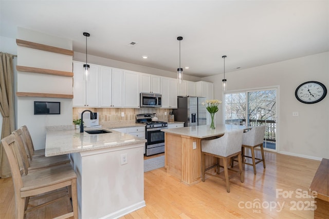 kitchen featuring stainless steel appliances, decorative backsplash, a sink, light wood-type flooring, and a kitchen bar