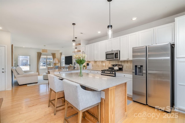 kitchen with light wood-type flooring, tasteful backsplash, stainless steel appliances, and open floor plan