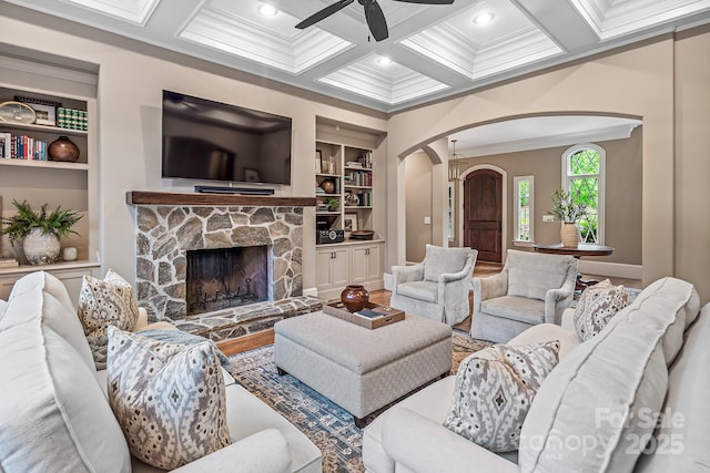 living room with crown molding, coffered ceiling, a fireplace, built in shelves, and beamed ceiling
