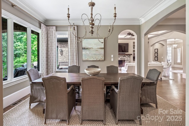dining space with a stone fireplace, plenty of natural light, ornamental molding, and wood-type flooring