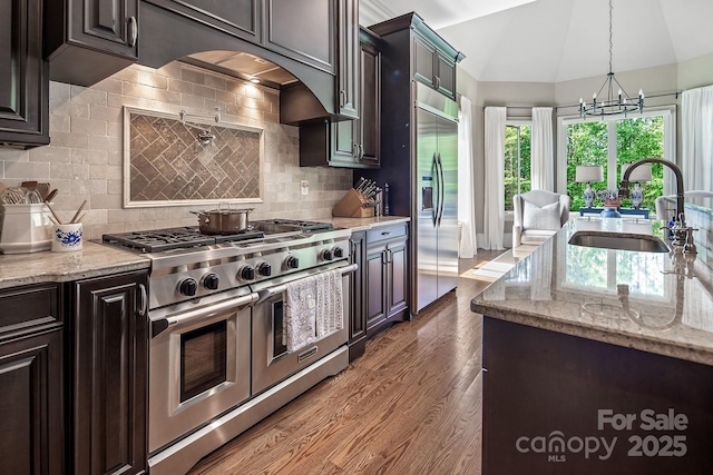 kitchen featuring sink, light stone counters, vaulted ceiling, dark brown cabinets, and premium appliances