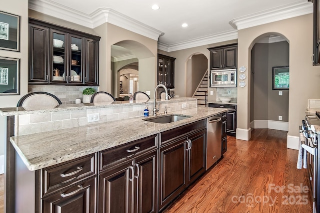 kitchen with sink, dark wood-type flooring, appliances with stainless steel finishes, dark brown cabinetry, and a center island with sink