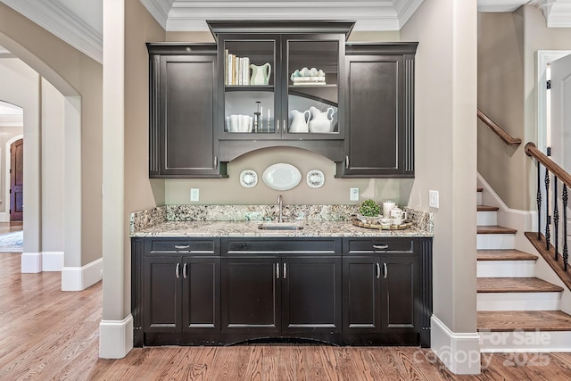 bar with crown molding, light stone countertops, sink, and light hardwood / wood-style flooring