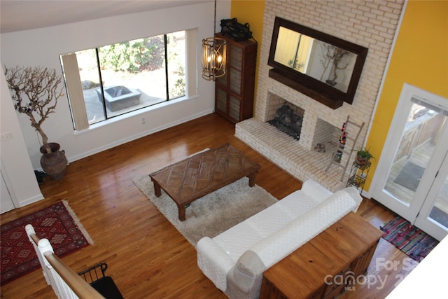 living room with a brick fireplace, a notable chandelier, baseboards, and dark wood-style flooring