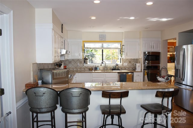 kitchen with white cabinets, appliances with stainless steel finishes, a sink, under cabinet range hood, and backsplash