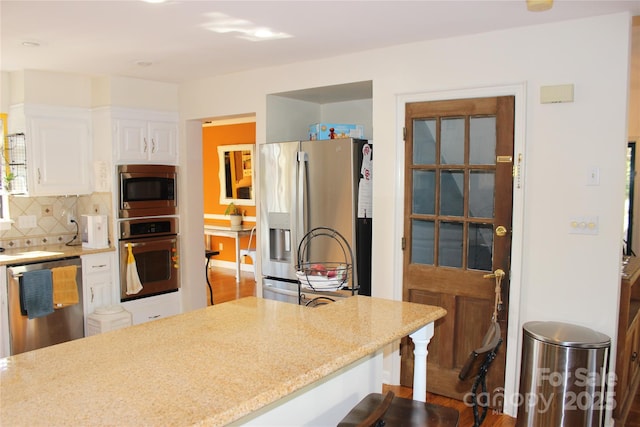 kitchen featuring white cabinets, decorative backsplash, light stone counters, a breakfast bar area, and stainless steel appliances