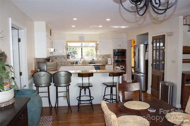 kitchen with white cabinets, a breakfast bar area, appliances with stainless steel finishes, light stone countertops, and a sink