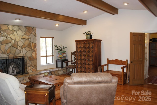 living area with vaulted ceiling with beams, a stone fireplace, and wood finished floors