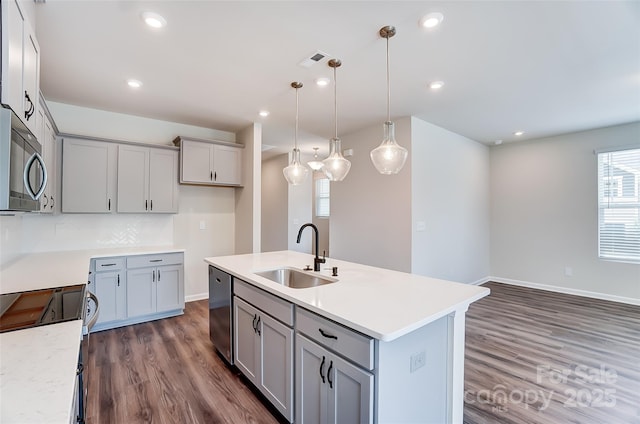 kitchen with sink, dark wood-type flooring, appliances with stainless steel finishes, an island with sink, and decorative light fixtures