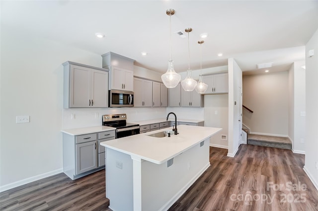 kitchen featuring gray cabinets, decorative light fixtures, sink, stainless steel appliances, and a center island with sink