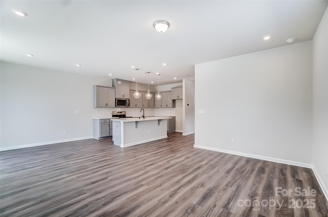 kitchen featuring gray cabinets, a kitchen island with sink, stainless steel appliances, dark hardwood / wood-style floors, and decorative light fixtures