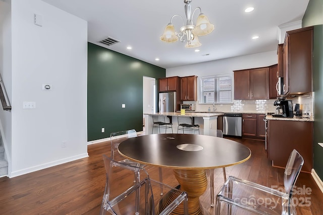 kitchen featuring appliances with stainless steel finishes, a kitchen island, decorative light fixtures, backsplash, and light stone counters