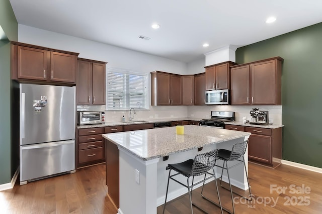 kitchen featuring sink, a breakfast bar area, light stone counters, a kitchen island, and stainless steel appliances