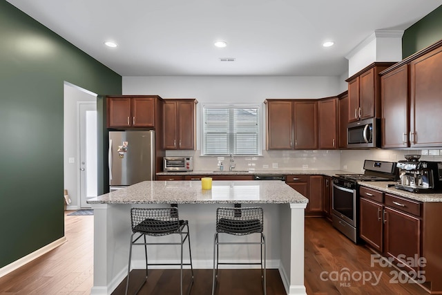 kitchen with a center island, a kitchen breakfast bar, stainless steel appliances, light stone countertops, and decorative backsplash