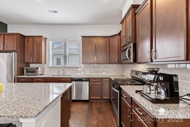 kitchen featuring sink, tasteful backsplash, dark hardwood / wood-style floors, stainless steel appliances, and light stone countertops