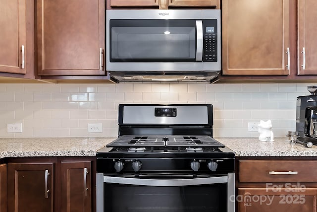 kitchen with black gas range, decorative backsplash, and light stone countertops