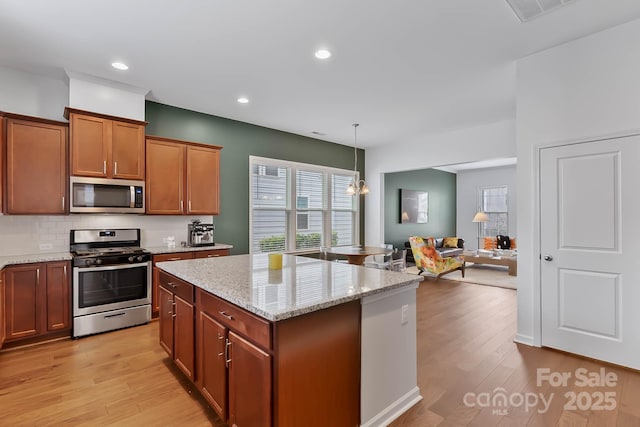 kitchen with plenty of natural light, hanging light fixtures, light hardwood / wood-style floors, stainless steel appliances, and light stone countertops