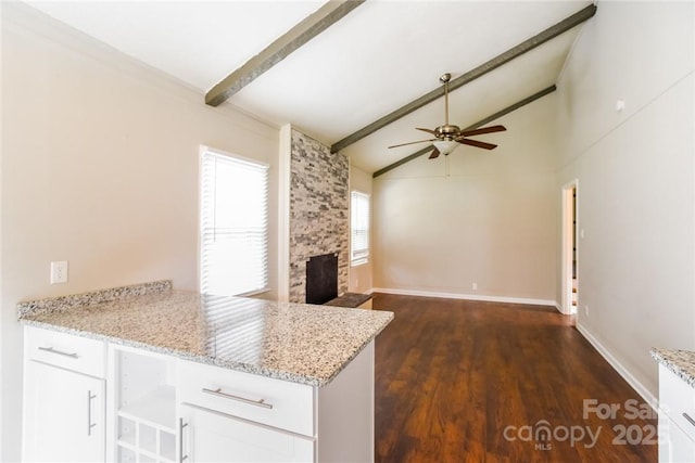 kitchen with light stone counters, a fireplace, lofted ceiling with beams, and white cabinets