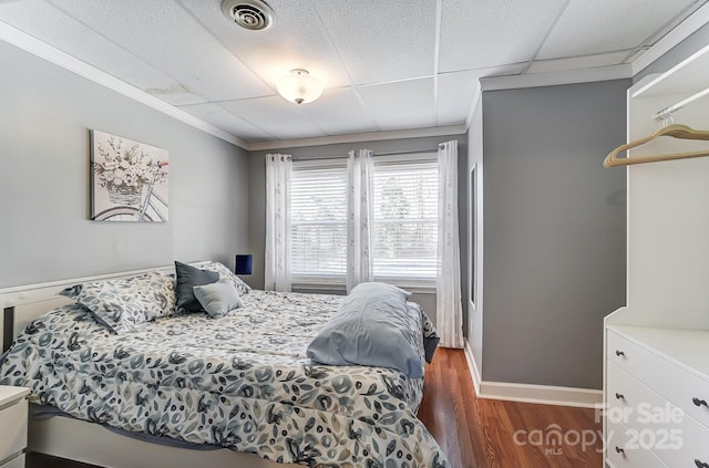 bedroom with dark wood-type flooring, crown molding, and a drop ceiling