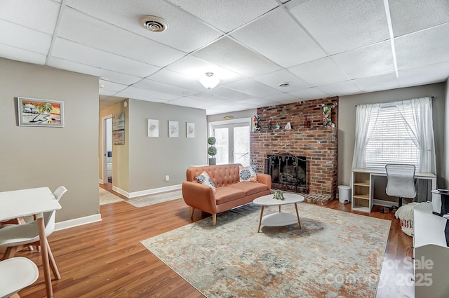 living room featuring a drop ceiling, hardwood / wood-style floors, a healthy amount of sunlight, and a brick fireplace