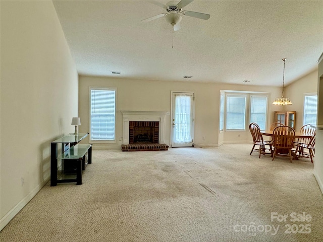 carpeted living room featuring a brick fireplace, ceiling fan with notable chandelier, and a textured ceiling