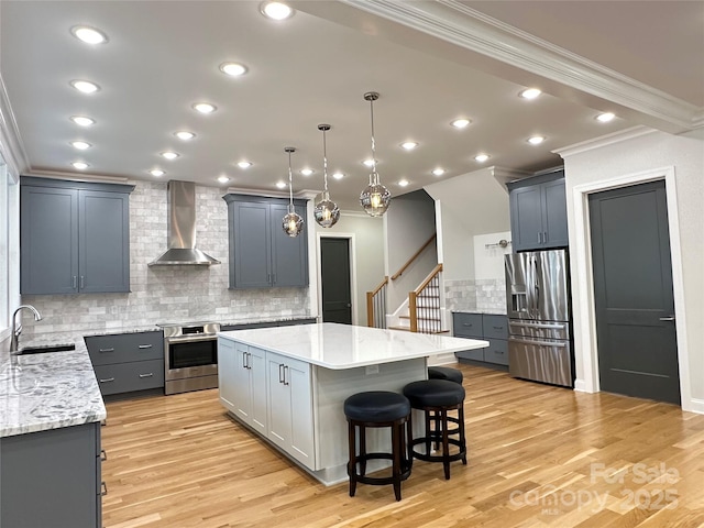 kitchen featuring sink, appliances with stainless steel finishes, light stone counters, a kitchen island, and wall chimney exhaust hood