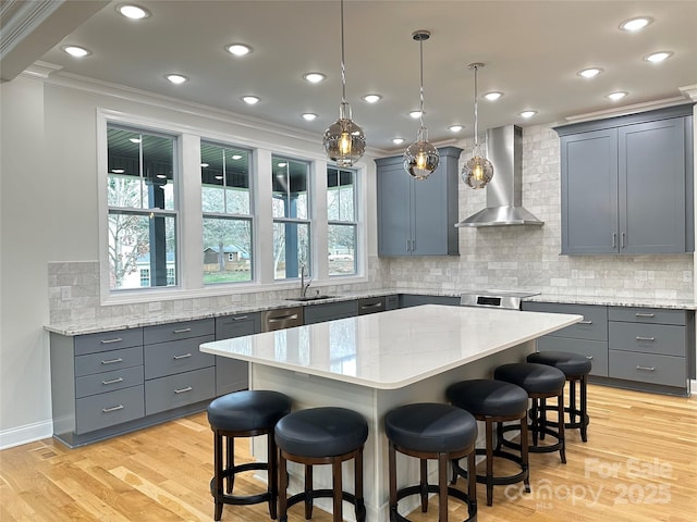 kitchen with sink, wall chimney range hood, decorative light fixtures, and a center island