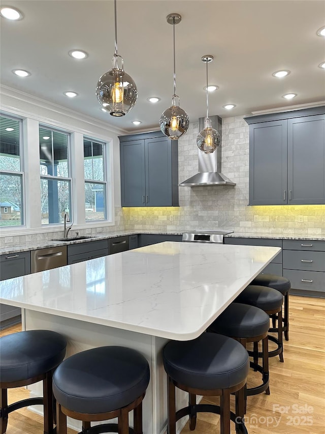 kitchen featuring wall chimney exhaust hood, a center island, sink, and hanging light fixtures