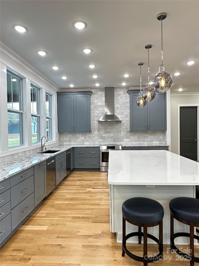 kitchen featuring sink, hanging light fixtures, stainless steel appliances, a kitchen bar, and wall chimney exhaust hood