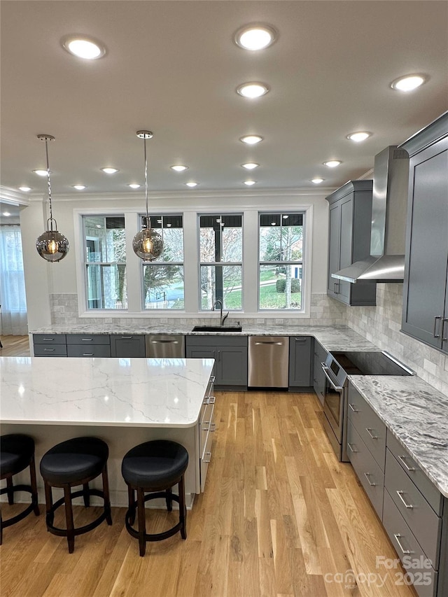 kitchen featuring light stone counters, stainless steel appliances, hanging light fixtures, and wall chimney range hood