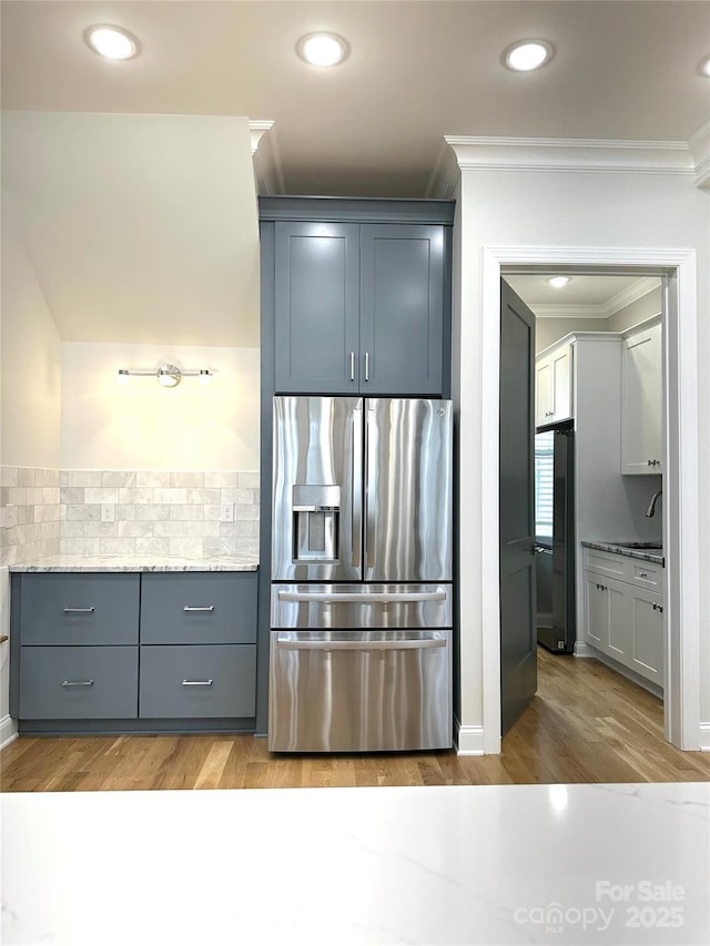 kitchen featuring tasteful backsplash, light hardwood / wood-style flooring, ornamental molding, stainless steel fridge, and light stone countertops