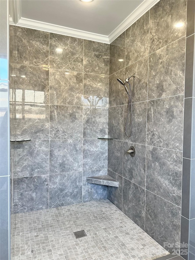 bathroom with ornamental molding and tiled shower