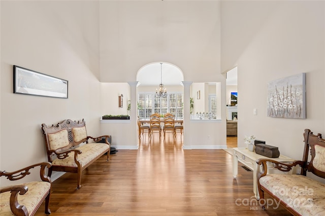 living area with decorative columns, baseboards, wood finished floors, a high ceiling, and a notable chandelier