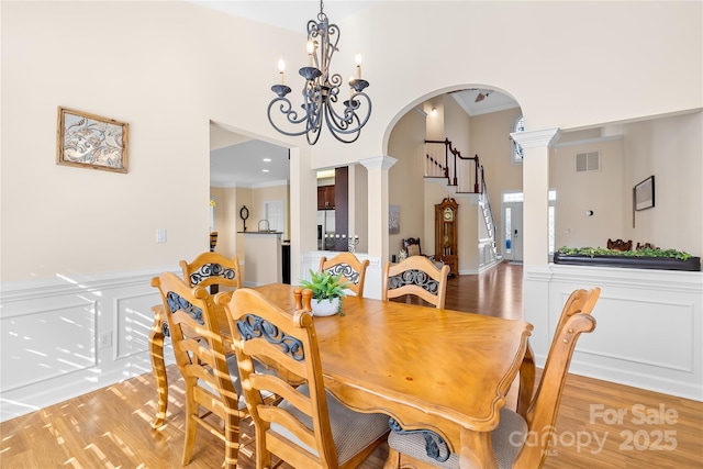 dining room with arched walkways, a high ceiling, ornamental molding, light wood finished floors, and decorative columns