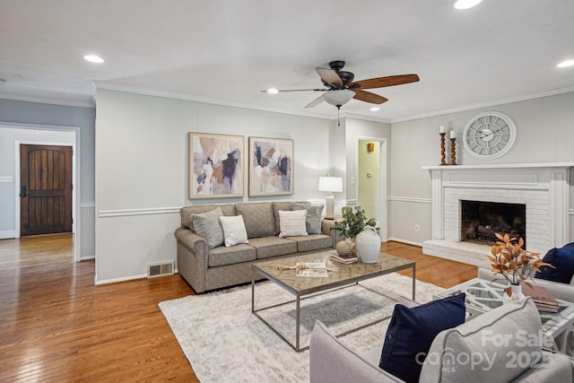 living area featuring wood finished floors, visible vents, baseboards, ornamental molding, and a brick fireplace