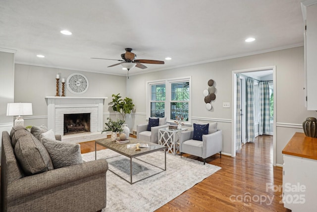 living room with a ceiling fan, wood finished floors, crown molding, a brick fireplace, and recessed lighting