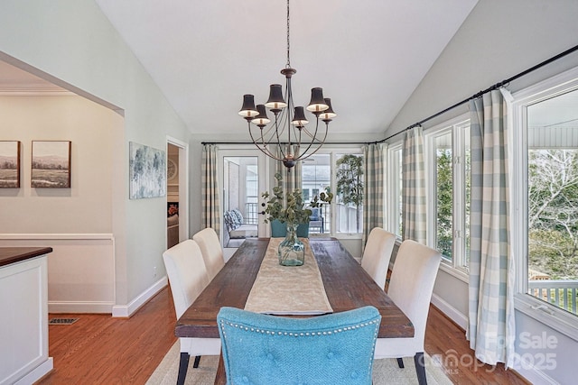 dining room with a wealth of natural light, lofted ceiling, light wood-type flooring, and an inviting chandelier